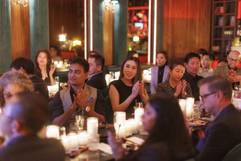Elegant event guests clapping at candlelit tables.