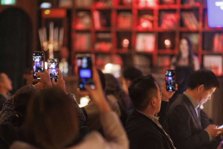 Audience recording speaker at event with smartphones.